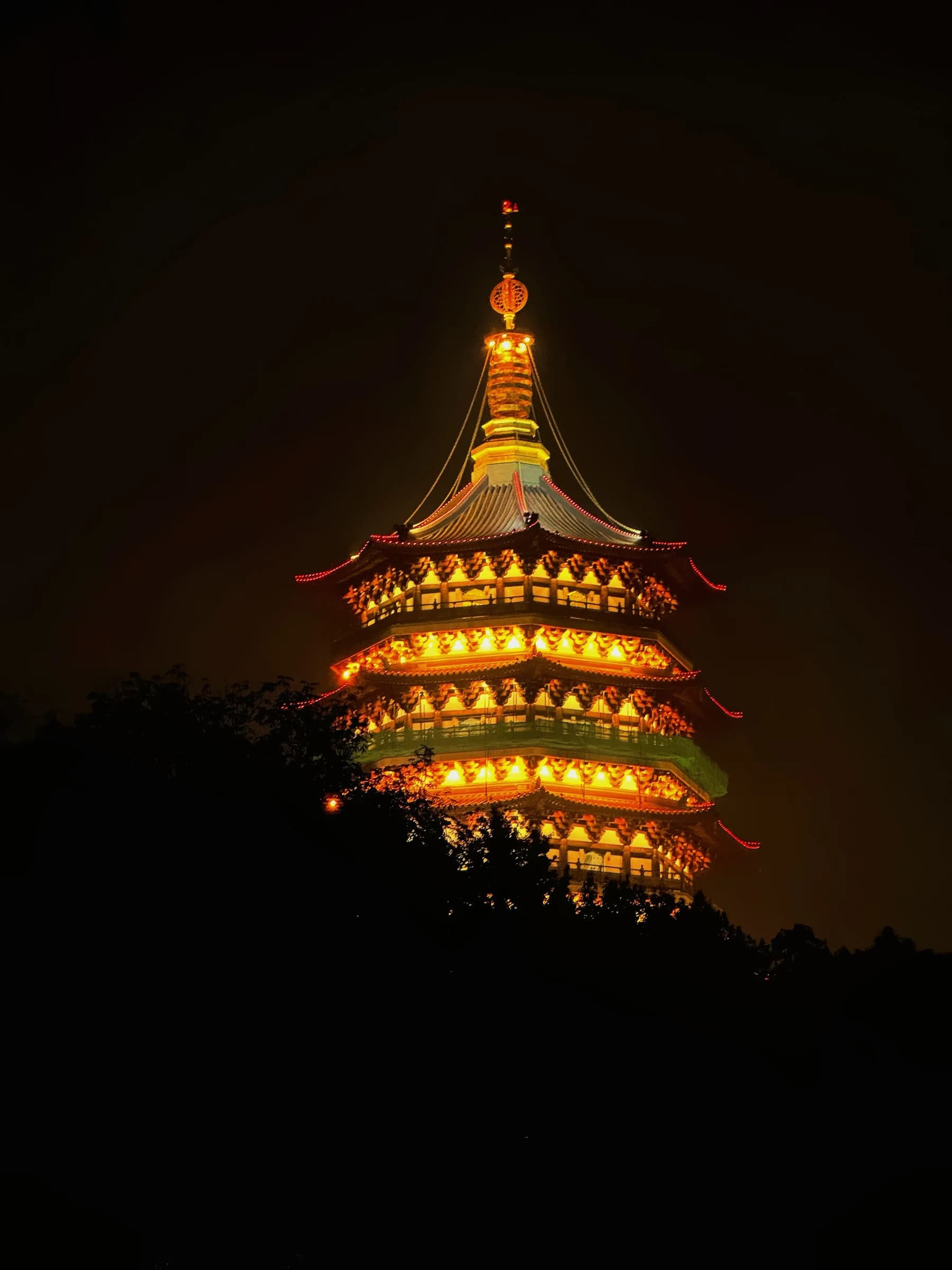 A warmly illuminated pagoda rises from a dark hillside at night